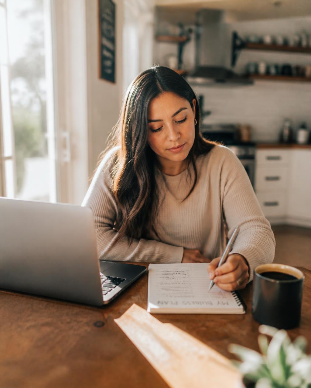 Founder planning her business steps at her kitchen table with a laptop and notebook